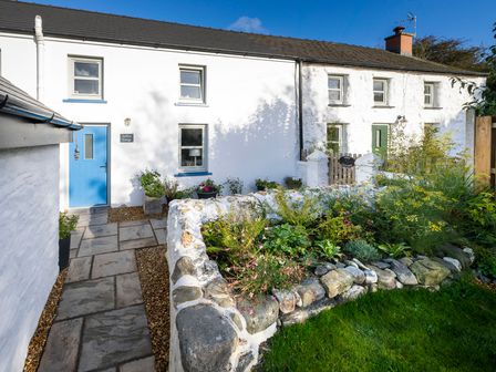 A stone cottage exterior with a blue door and a garden with stone wall at Dyffryn Cottage in Aberporth