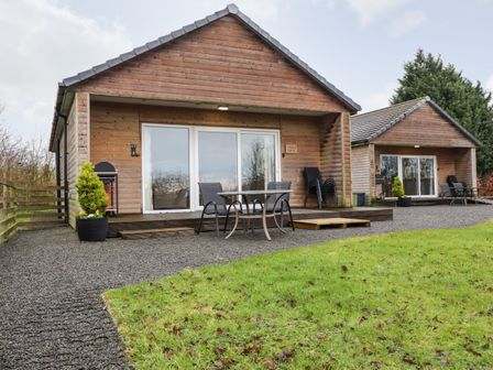 Two wooden lodges with glass sliding doors outdoor seating and potted plants in front at Oak Lodge in Goosnargh
