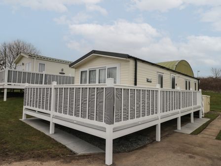 A mobile home with a white railing and a paved pathway at Rowan Court 2 in Cayton