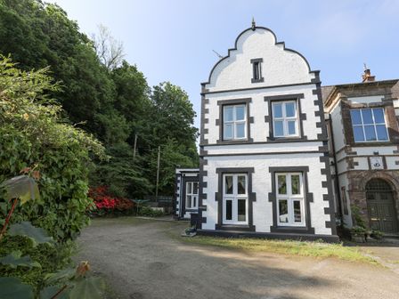 A white and black two-story brick house with multiple windows next to greenery and a gravel area at Llys y Graig in Pentraeth