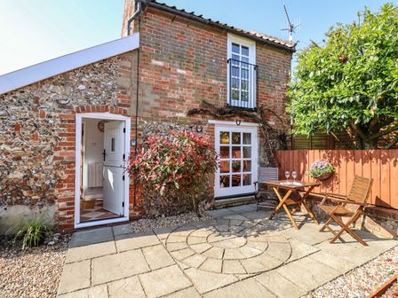 An outdoor patio area with a wooden table and two chairs next to a brick and flint wall at Admiral Cottage in Blaxhall near Snape Suffolk