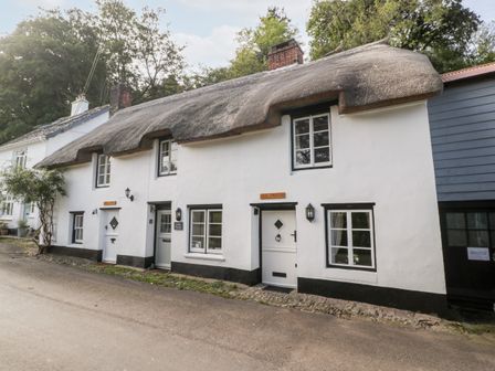 A row of white cottages with thatched roofs along a street at The Old Thatch in Porlock