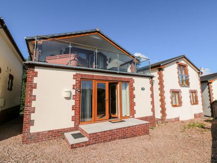 The exterior of a two-story house with glass balcony railing and wooden framed doors at Hazelwood Lodge in High Bickington