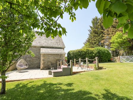 An outdoor patio area with seating furniture a hanging chair a stone building and green lawn at St Marks School House in Nant-Glas near Rhayader