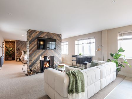 A living room with a beige sofa a round dining table and a TV mounted on a wooden feature wall at The Hayloft in Llanfechell