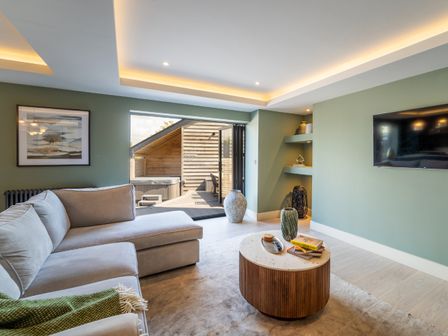 A living room with a sectional sofa a round coffee table and a wall mounted television at The Farmhouse in Llanfechell