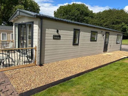 A beige mobile home with a patio and outdoor chairs at Ambleside in Cullompton
