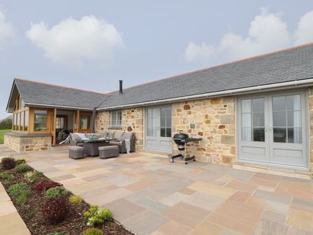 An outdoor patio with seating furniture and a barbecue next to a stone cottage at Trevilges Cottage in Trewennack near Helston