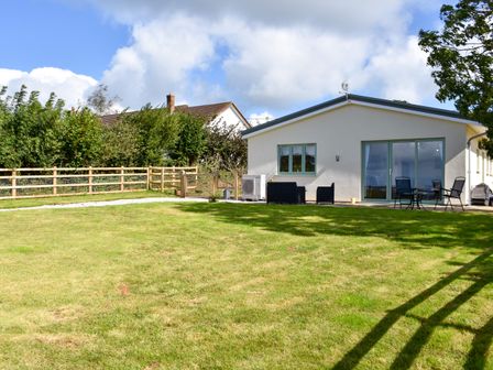 A backyard with a lawn a wooden fence patio furniture and a house with large windows at The Linhay in Lapford