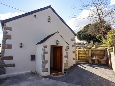 The exterior of a white stone building with an open wooden door and a small outdoor seating area with a table and two chairs at The Old Chapel in Ilsington