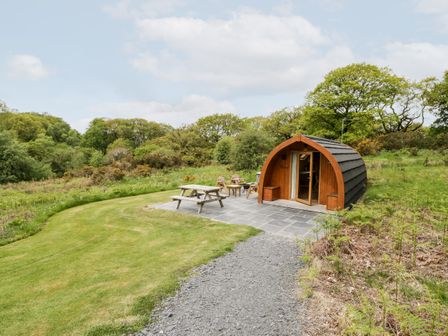 A wooden pod with patio furniture on a stone terrace surrounded by grass and trees at Llugwy Pod in Capel Garmon near Betws-Y-Coed
