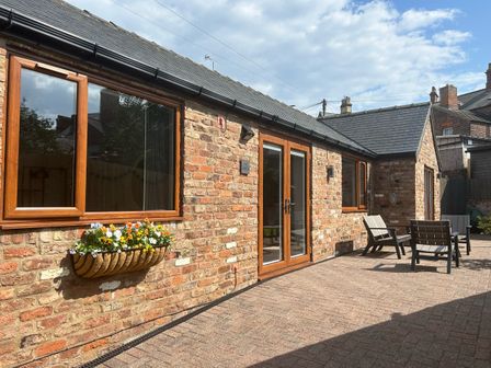 An outdoor patio area with brick walls wooden framed windows and doors a flower box with flowers and outdoor chairs at The Annexe in Bridlington