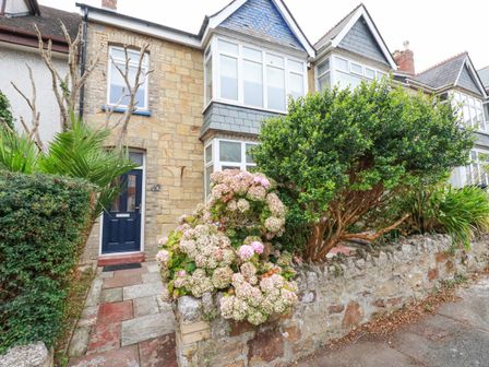 The front of a stone house with a blue door and bay windows surrounded by various bushes and flowers at Serendib Cottage in Newquay
