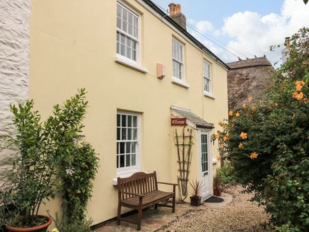 The exterior of a yellow house with white framed windows a wooden bench and plants at Ellenor in Malborough