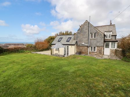 A house with a large green lawn and patio umbrella in the garden with ocean view at Ivy Cottage Trenale near Tintagel