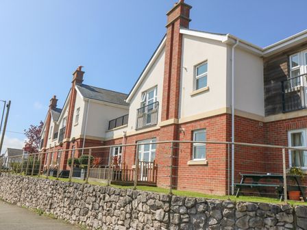 A row of modern residential houses with brick and cream siding and a stone retaining wall in front at Sea La Vie in Benllech