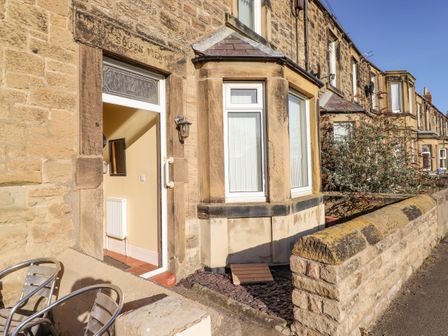 Stone terraced houses with bay windows and an open door showing an interior hallway with a radiator and mirror at Southview Amble in Amble