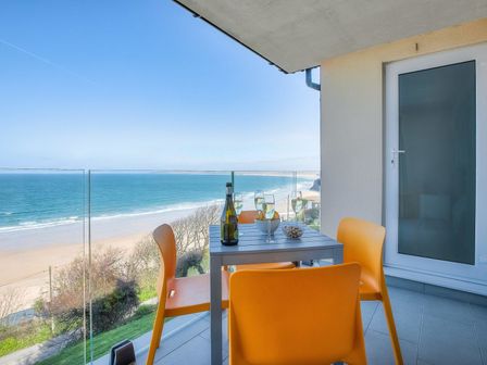 A balcony with a table and orange chairs overlooking the ocean at Cirrus in Carbis Bay