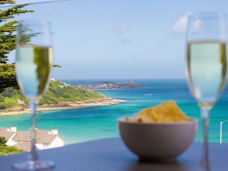 A coastal view with two glasses of champagne and a bowl of chips on a table at Sandsifters II in Carbis Bay