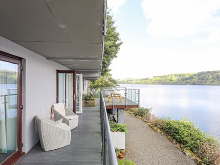 A balcony with two chairs and a table overlooking a lake and hills at Tegid Lakeside - Bala Lake