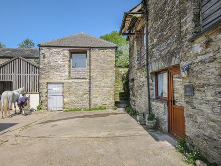An outdoor area with stone buildings and a person tending to a white horse at Mill House in Lostwithiel near Pelynt