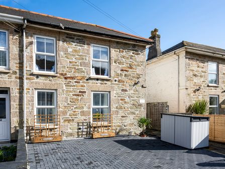A stone exterior of a two-story house with four windows and a front yard with a wooden storage box at Beachspoke Loft in Portreath