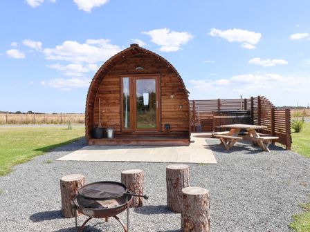 A small wooden cabin with glass doors a picnic table a wood fire pit with log seats and a hot tub in an outdoor area at Husk Little Kelk near Bridlington