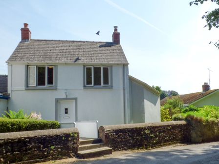 A two story house with two chimneys and three windows surrounded by a stone wall at Spring Garden Cottage in Laugharne