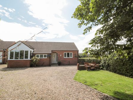 A brick house with a front door three windows a gravel driveway and two wooden chairs on a lawn at Church View in Withernwick near Aldbrough