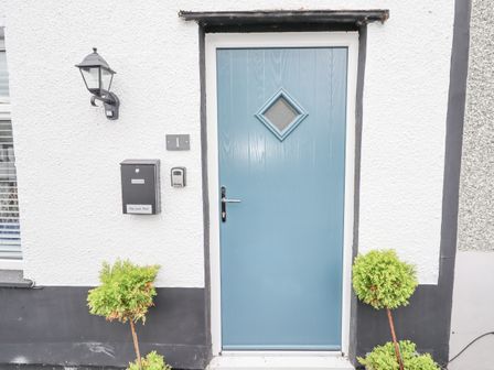 A blue front door with diamond window and black mailbox on white wall with two small plants at Sea View Terrace in Conwy