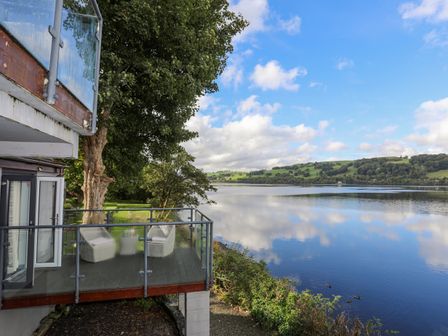 A balcony with table and chairs overlooking a lake with trees and hills at Drysgol Lakeside Bala Lake in Bala