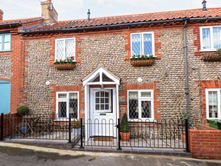A stone and brick terraced house with white framed windows and door and a small fenced front patio at Seaspray in Sheringham