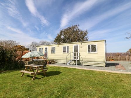 A mobile home with a picnic table and umbrella on a lawn at Cwrt y Ceffyl in Boduan near Morfa Nefyn