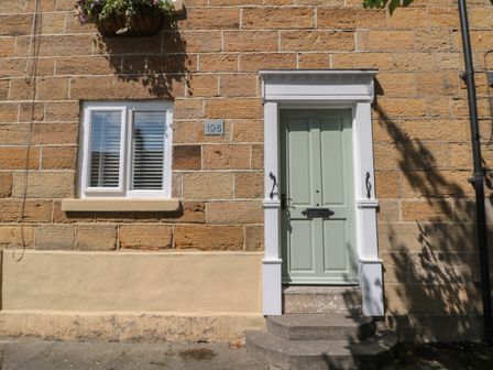 A green door with white trim and steps next to a window with white shutters on a stone wall at 106 Westgate in Guisborough