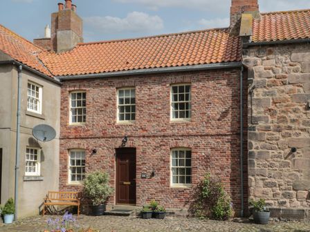 A brick house with a tiled roof and potted plants in front at Charter's Cottage in Berwick-Upon-Tweed