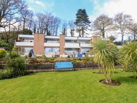 A building with balconies overlooking a garden with a blue bench and palm trees at Sunny View in Dawlish Warren