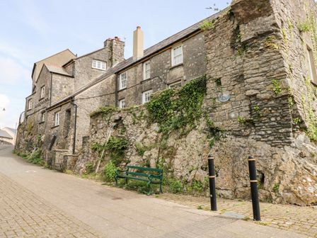 A stone building with white windows and a green bench on a paved street at 10 Westgate Hill in Pembroke