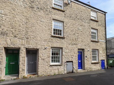 A stone exterior of a building with green gray and blue doors and white framed windows at 4 Martindales Yard in Kendal
