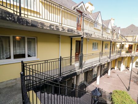 An exterior view of a yellow apartment building with black railings and staircase at 2 Garnish Court in Glengarriff County Cork