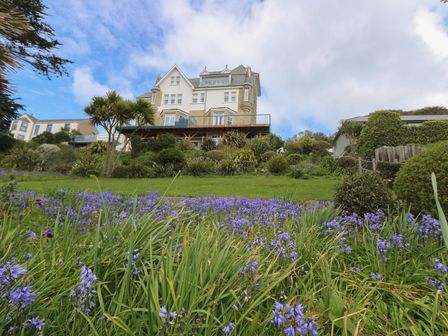 A garden with purple flowers in front of a large white house with multiple windows and a balcony at The Tower 5 Corisande Manor in Newquay
