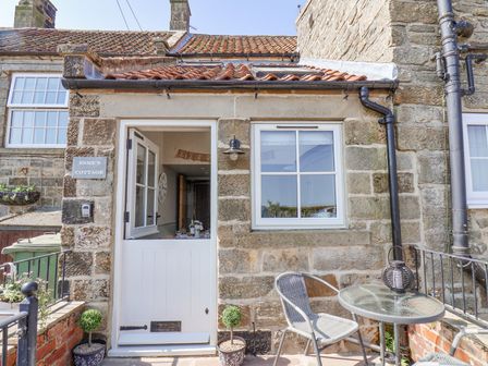 Stone cottage exterior with a half open white door a white framed window and a small outdoor table and chairs at Esme's Cottage in Ugthorpe near Whitby