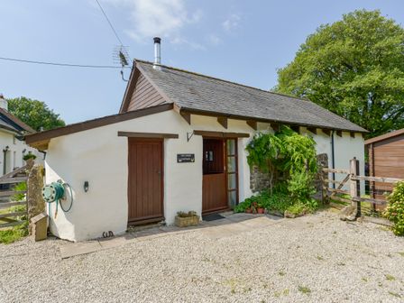 A small white cottage with wooden doors and plants outside at Two Shoes Cottage Sourton near Sourton Down