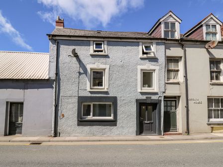 A grey two-story house with black door and four windows on a street at Lane Cottage in Cardigan