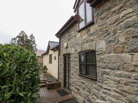 A stone and brick house exterior with windows and a door next to green bushes at The Searle in Nantmel near Rhayader