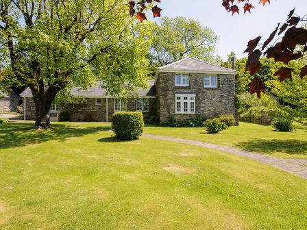 A stone house with white windows surrounded by trees and lawn at Byre Trethin near Camelford