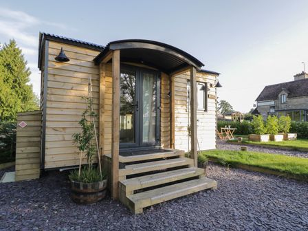 An exterior view of a wooden cabin with steps leading to a glass door at Beech in Kemble