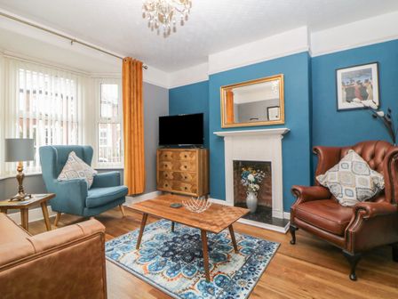 A living room with two armchairs a wooden coffee table a TV on a wooden cabinet and a fireplace at Cornerside in Sidmouth