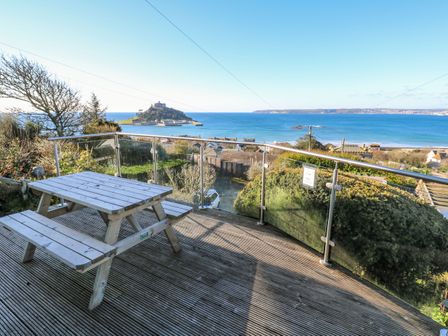 A wooden picnic table on a balcony with glass railing overlooking the sea and an island at Rosemount in Marazion