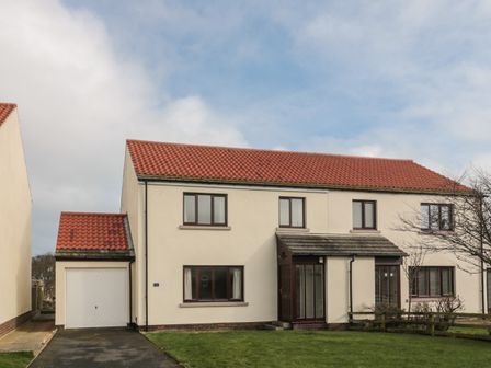 A two-story semi detached house with a red tiled roof garage and front lawn at Causeway Cottage in Holy Island