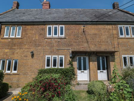 A stone house with two white front doors and multiple windows with a garden in front at Stonecutter's Cottage in Stoke-Sub-Hamdon Somerset